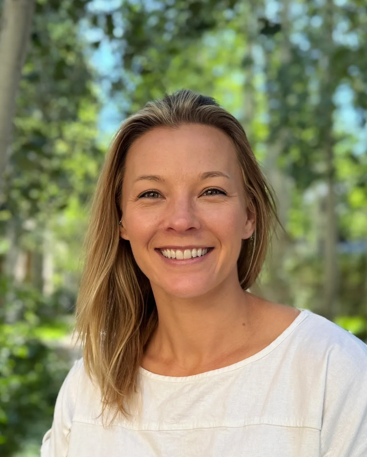 Lauren Snyder, Executive Director of the People First Behavioral Health Alliance — outdoor portrait, smiling, with sunlit aspen leaves behind her.